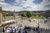 A view of Stuttgart's Schlossplatz square in summer. The sky is blue, the trees are green, people are milling around the square and enjoying the good weather. On the left edge of the picture the Königsbau, on the right the Kunstmuseum.